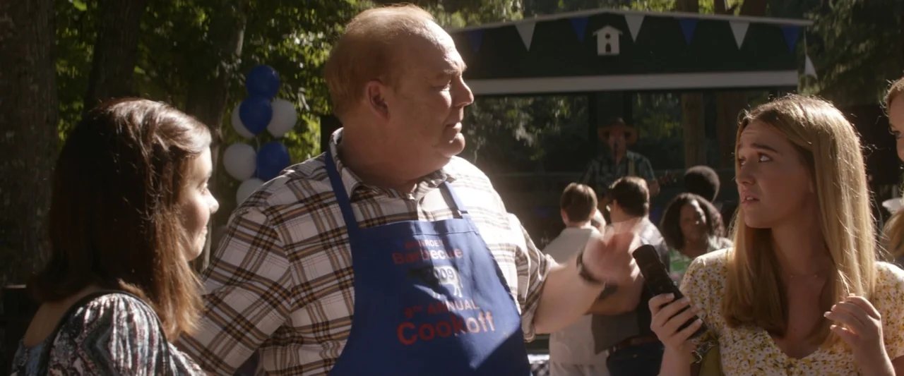 On a Wing and a Prayer (2023) movie still: medium — An outdoor festival area features a small covered stage with blue and white bunting. A…