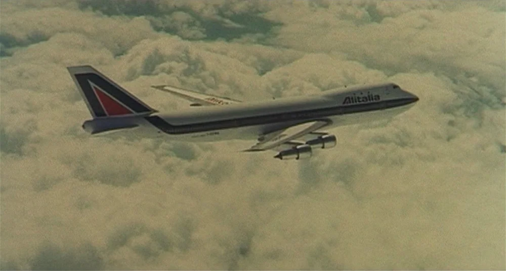 Footprints (Le Orme) (1975) movie still: wide — A commercial passenger jet cruises above a vast expanse of white cumulus clouds. The aircraft…