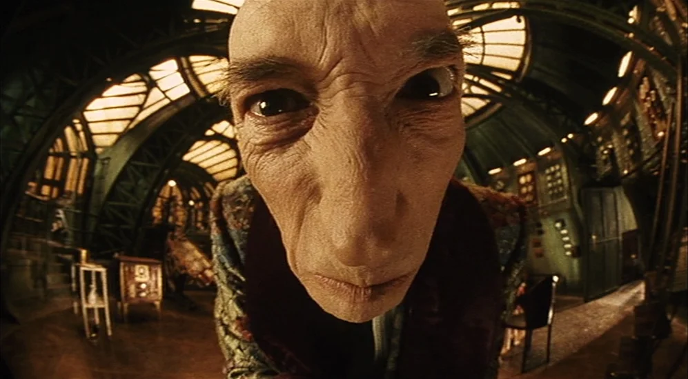 The City Of Lost Children movie still: closeup — An interior laboratory with metallic vaulted structures and warm glowing light fixtures above. An…