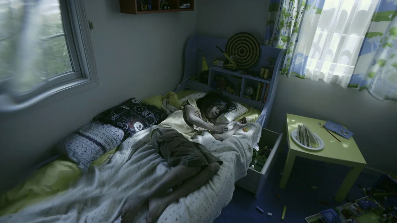 Confessions (2010) movie still: medium — A cluttered child's room features toys, a small yellow table, and a bed. A young girl lies on the bed while…