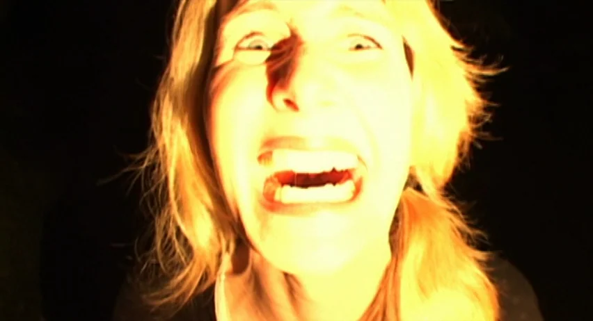 Inland Empire (2006) movie still: closeup — A woman's face is illuminated by a harsh, low-angle light source in darkness. Her mouth is held open…