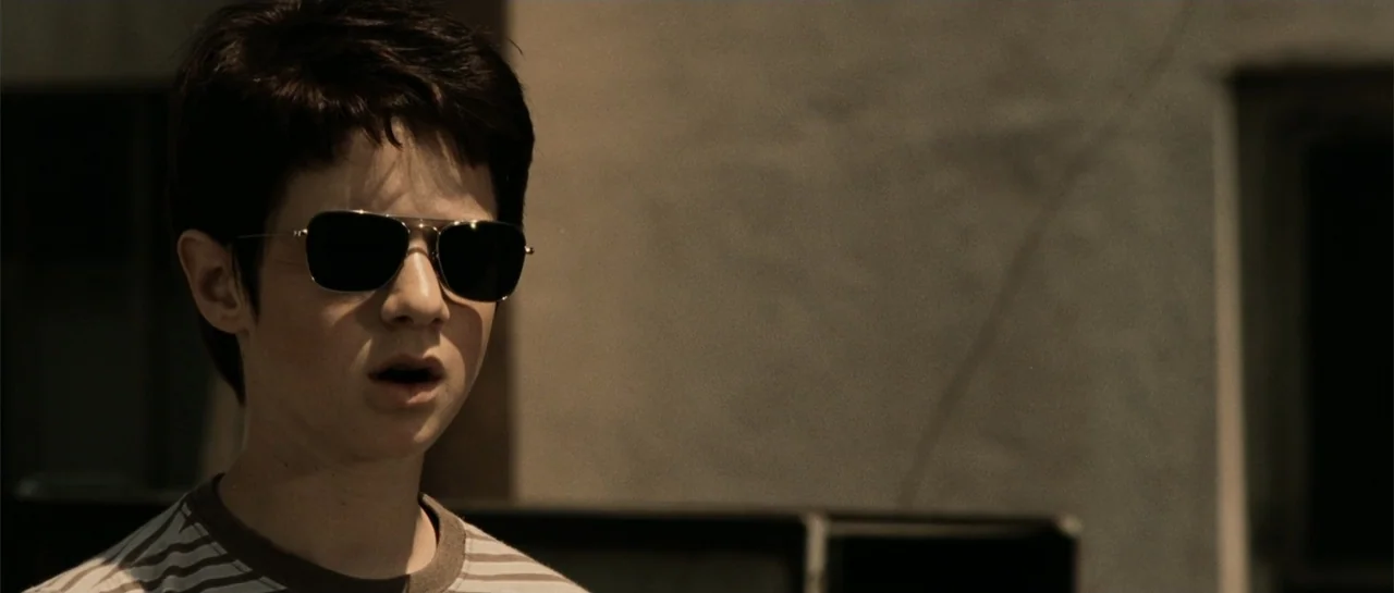 Daredevil (2015) movie still: closeup — A teenage boy stands outdoors against a blurry concrete surface. He wears dark aviator sunglasses while…