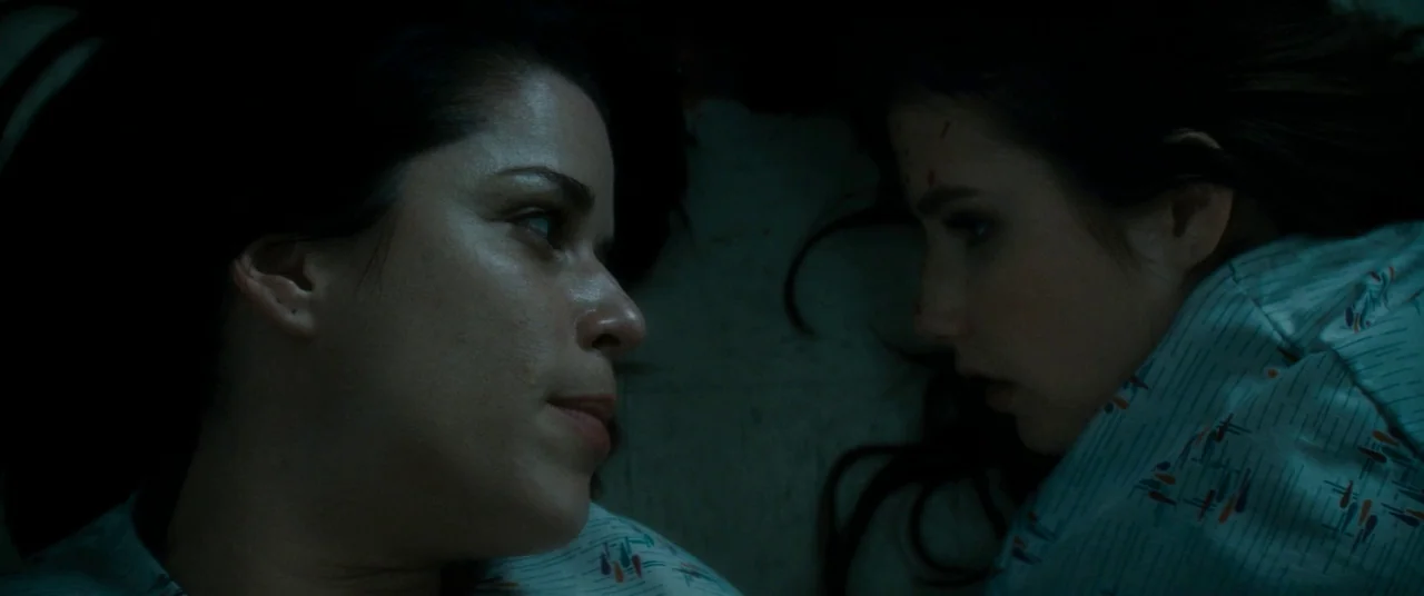 Scream 4 (2011) movie still: closeup — Two women lie side by side on a sterile surface in low lighting. They face each other while wearing matching…