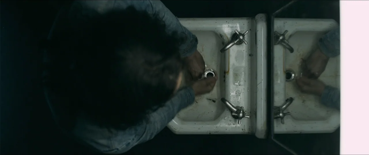 Woman of the Hour (2024) movie still: medium — A top-down view shows a white ceramic basin with metallic taps and rust stains. A person wearing a…