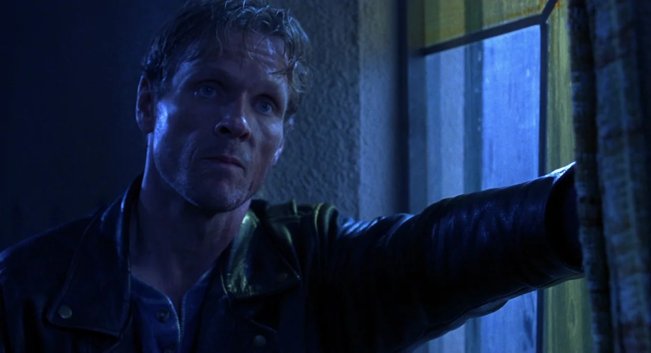 Tales from the Crypt: Demon Knight (1995) movie still: closeup — A man stands in a dark room illuminated by cold light from a window. He leans his…