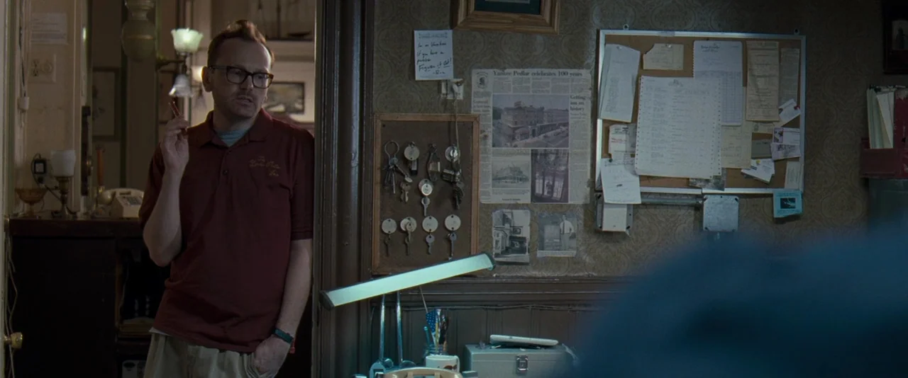 The Innkeepers (2011) movie still: medium — A hotel front desk area features cork boards covered with papers, keys, and newspaper clippings. A man…