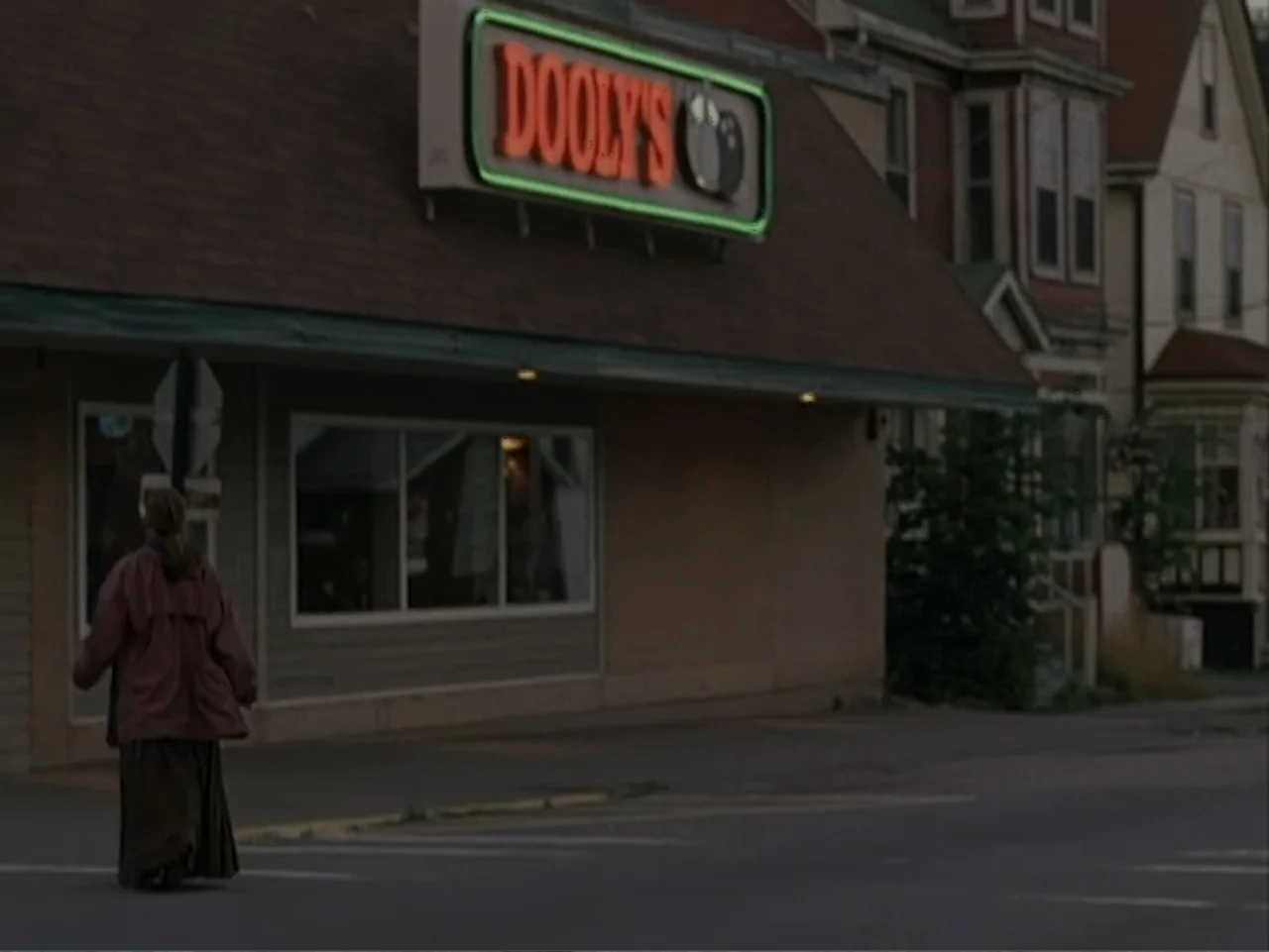 Catch a Falling Star (2000) movie still: fullbody — A single-story commercial building features a prominent glowing neon sign overhead. A lone woman…