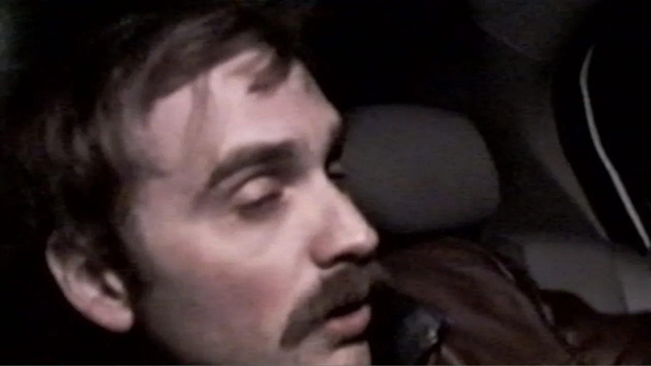 S-V/H/S: Un cortometraje de Las Crónicas del Miedo (2023) movie still: closeup — A dimly lit car interior at night with visible digital video noise…