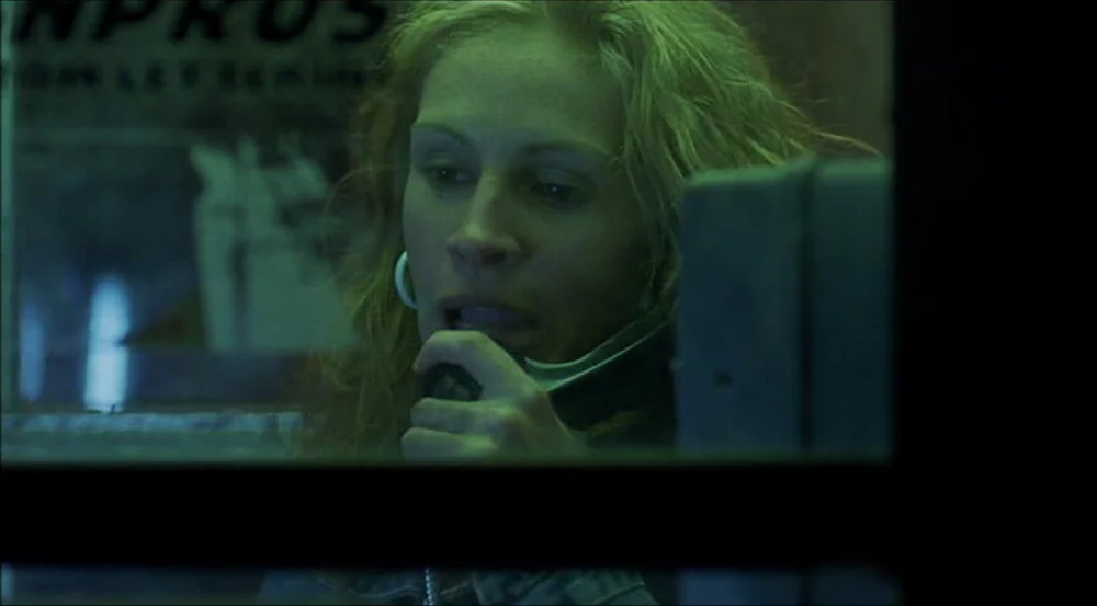 Erin Brockovich (2000) movie still: closeup — A dimly lit phone booth at night is bathed in an intense green light. A woman with wavy blonde hair…