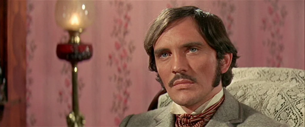 Far from the Madding Crowd (1967) movie still: closeup — A man sits in a room with floral pink wallpaper and a lace-covered chair. He remains still…