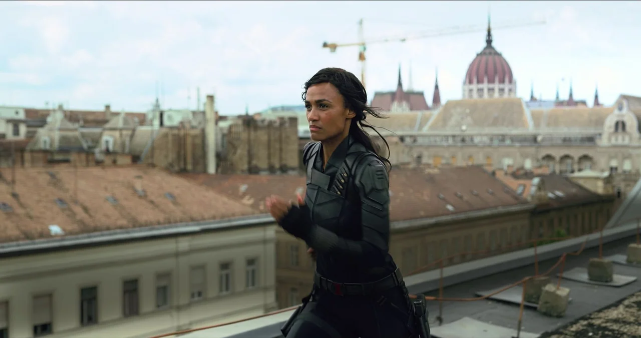 Black Widow (2021) movie still: medium — A woman runs across a sprawling rooftop with city buildings visible in the distance. The Hungarian…