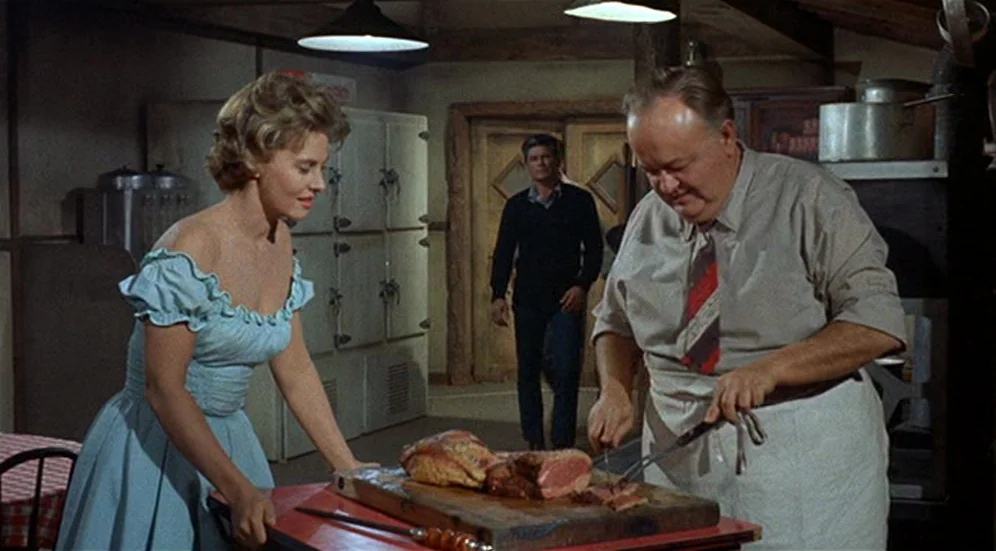 Kid Galahad (1962) movie still: medium — A rustic restaurant kitchen features industrial metal refrigerators and a wooden prep table. A chef carves…