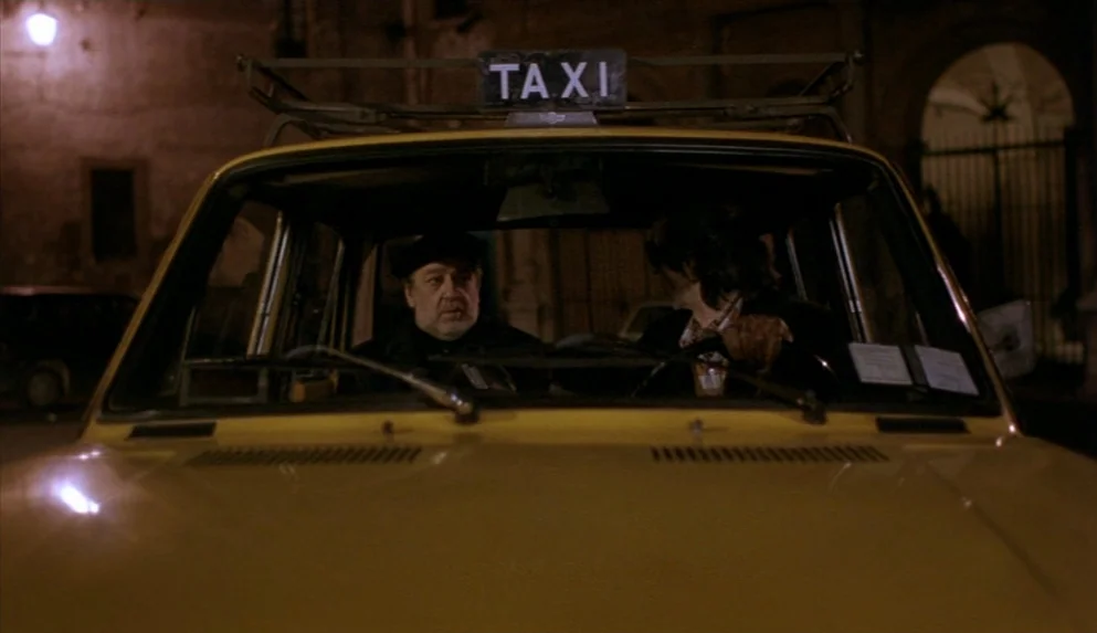 Night on Earth (1991) movie still: medium — Two men sit inside a parked yellow taxi at night on a city street. The taxi is parked on a…