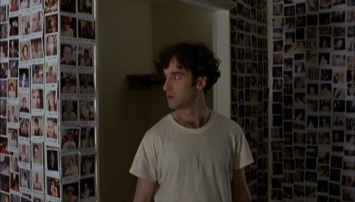 Highway 61 (1991) movie still: medium — Walls of an apartment are densely covered with hundreds of small square photographs. A young man wearing a…