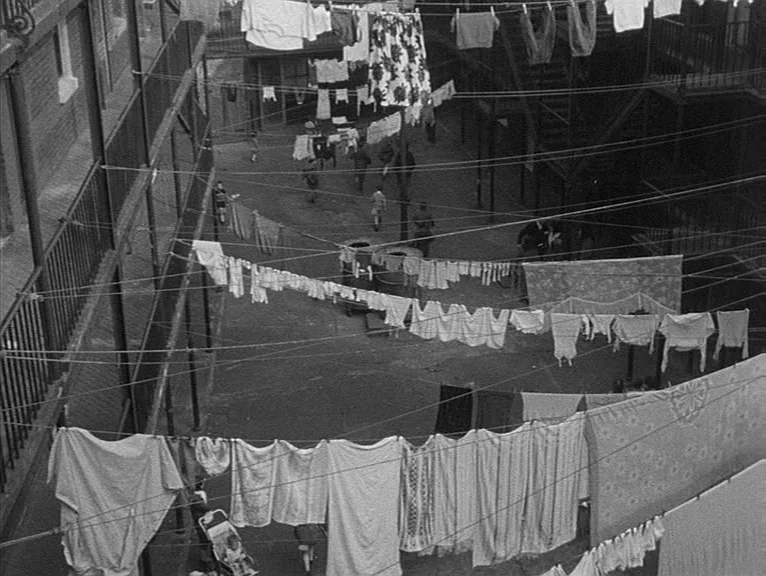 Cathy Come Home (1969) movie still: establishing — A dense urban tenement courtyard features multiple levels of iron balconies and staircases.…
