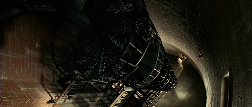 Shutter Island (2010) movie still: wide — A dark, cylindrical brick tower contains a prominent, ornate metal spiral staircase. The wide perspective…