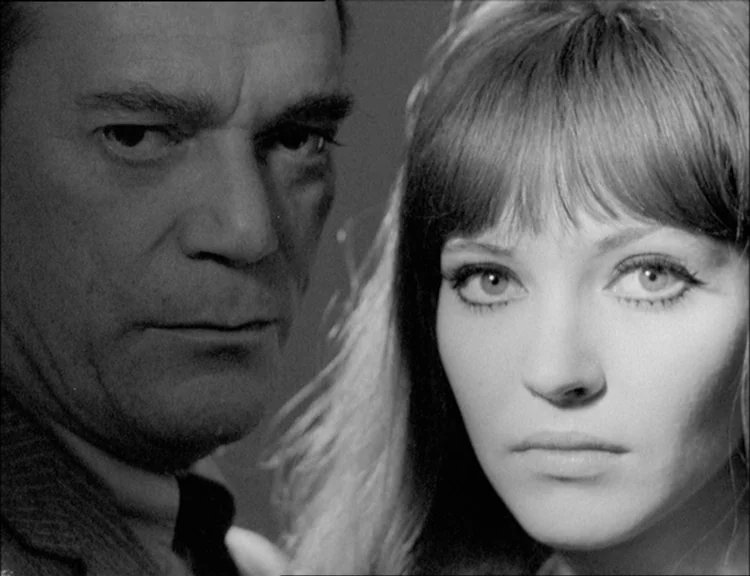 Alphaville (1965) movie still: closeup — An interior space provides a neutral, featureless backdrop for the subjects. A man and a young woman are…