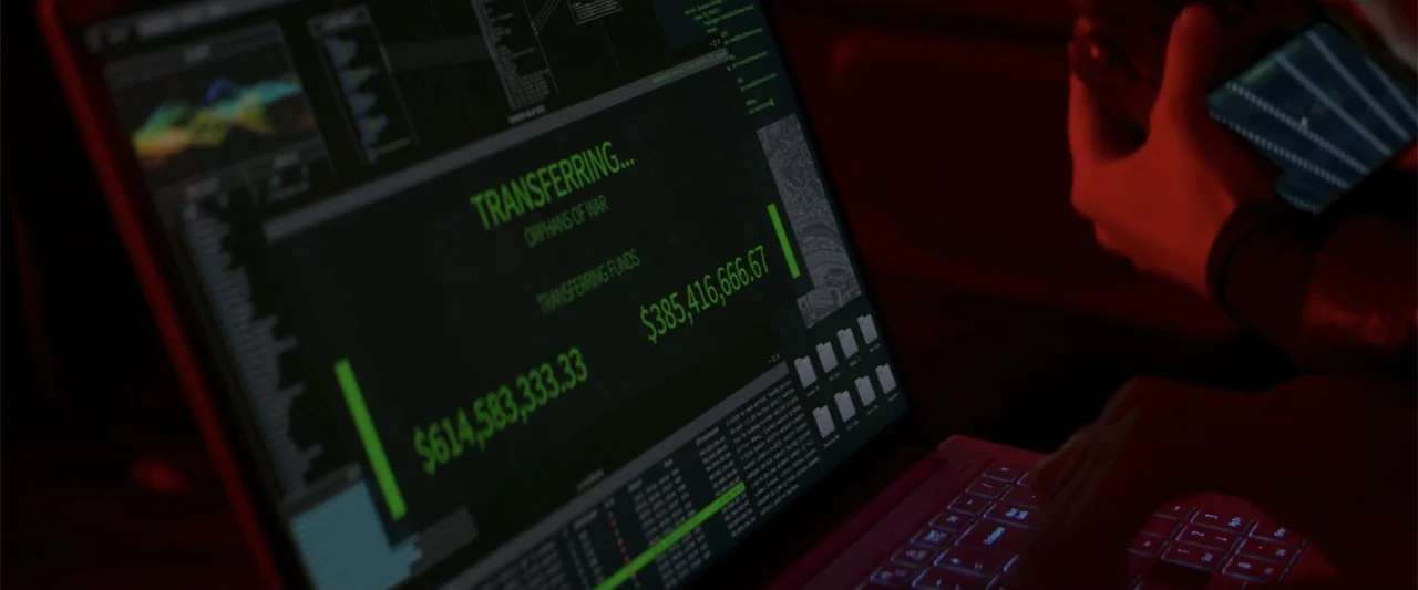 Operation Fortune: Ruse de Guerre (2023) movie still: closeup — A dimly lit room focuses on a laptop screen displaying a digital financial transfer…