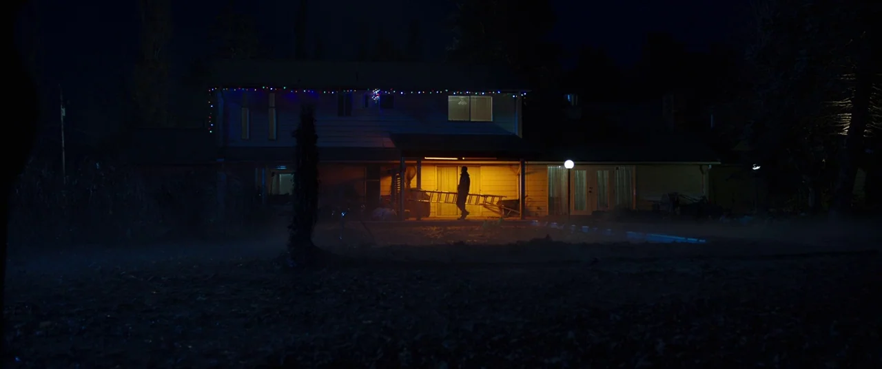 Child's Play (2019) movie still: wide — A two-story suburban house features strings of lights along the roof at night. A lone man stands under the…
