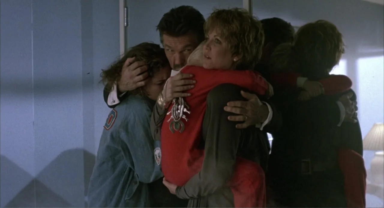 Poltergeist III (1988) movie still: medium — A group of people stand together within an interior space with a wall mirror. The central male and…
