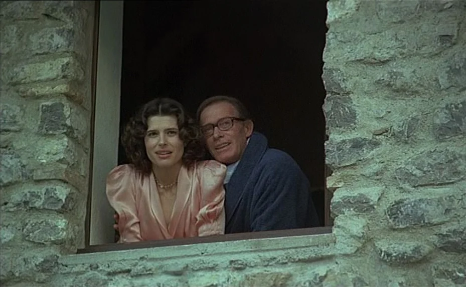 The Woman Next Door (1981) movie still: medium — A man and woman lean through a window in a rustic stone building. The couple rests their arms on…