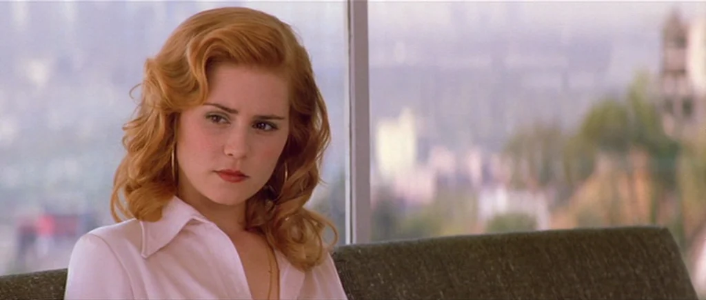Where The Truth Lies (2005) movie still: medium — A woman sits in a chair in front of a floor-to-ceiling glass window. She gazes off-camera while…