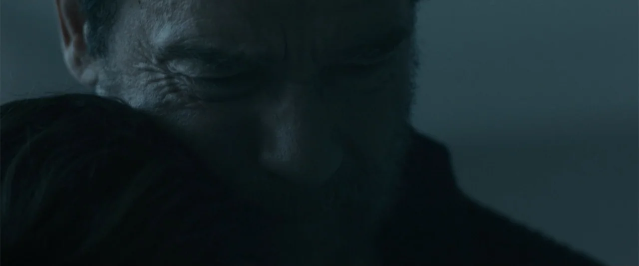 Maggie (2015) movie still: closeup — A dark and indistinct setting provides a backdrop for a tight, close-up embrace. A middle-aged man with a…