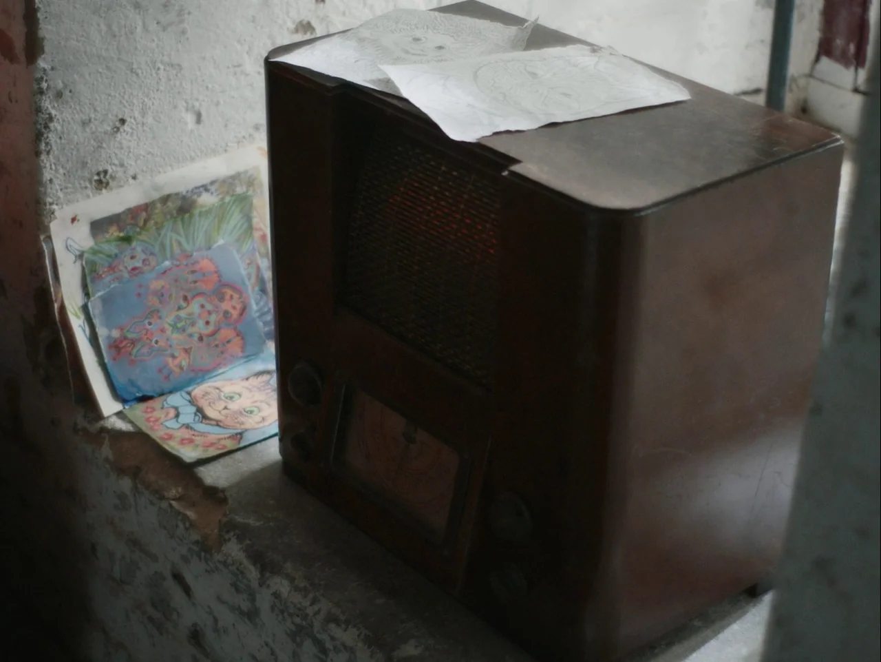 The Electrical Life of Louis Wain (2021) movie still: closeup — A dark wooden vintage radio sits on a concrete ledge against a textured wall.…