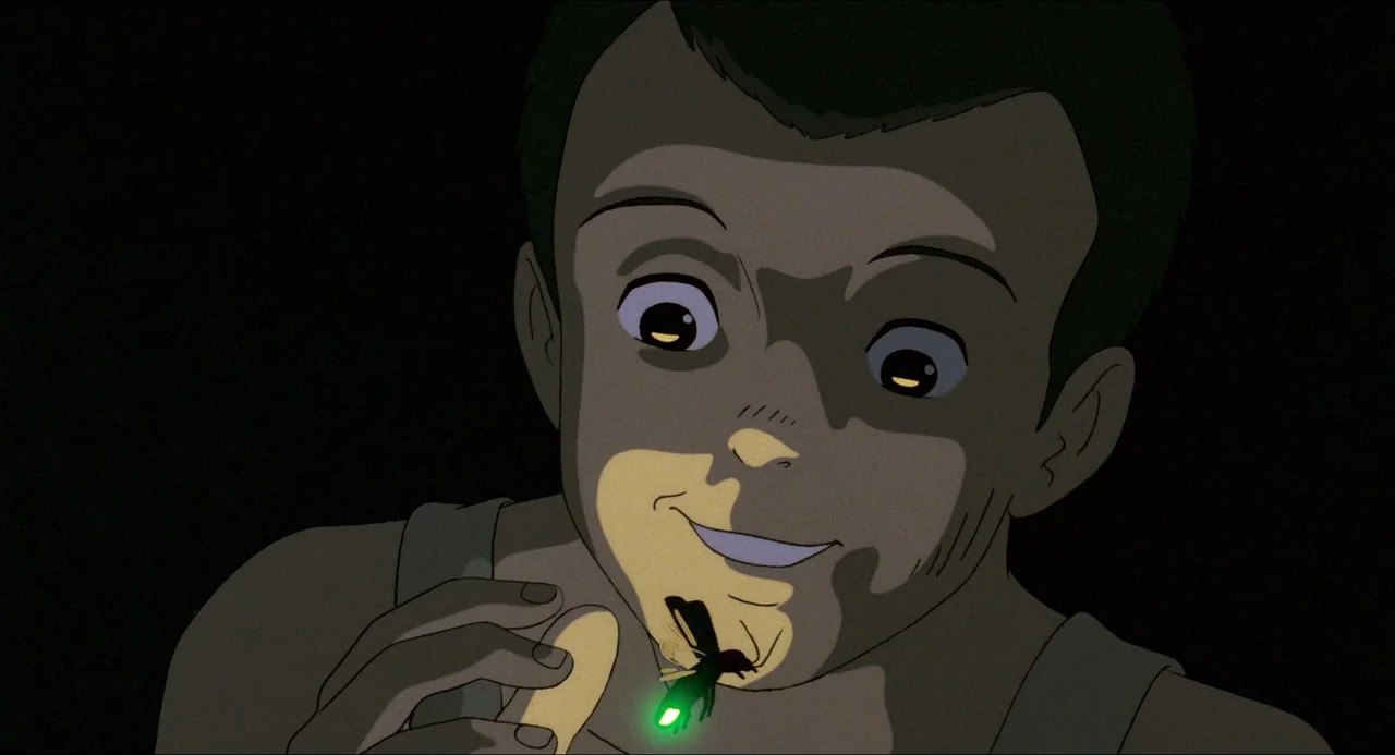 Grave of the Fireflies (1988) movie still: closeup — A dark, nondescript room serves as the setting for this quiet moment. A young boy smiles while…