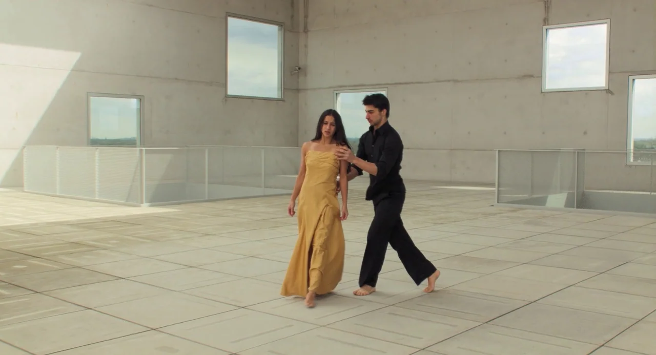 Pina (2011) movie still: fullbody — A minimalist hall features polished concrete panels, high square windows, and light grey mesh railings. A man…