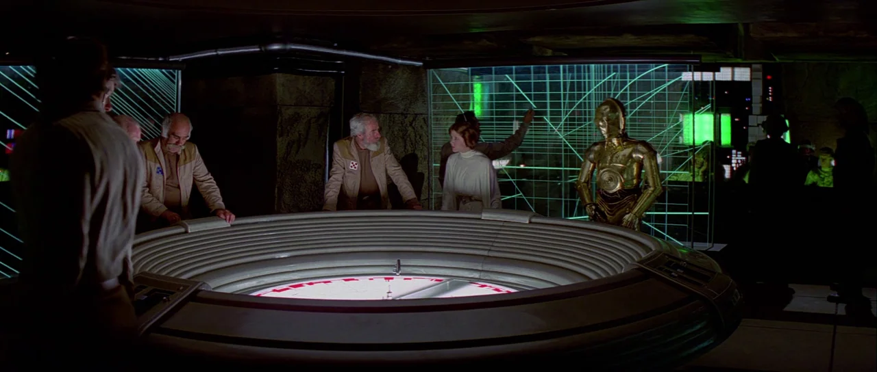 Star Wars (1977) movie still: wide — A dark command room features a large circular light table and glowing green grid displays. Several figures…