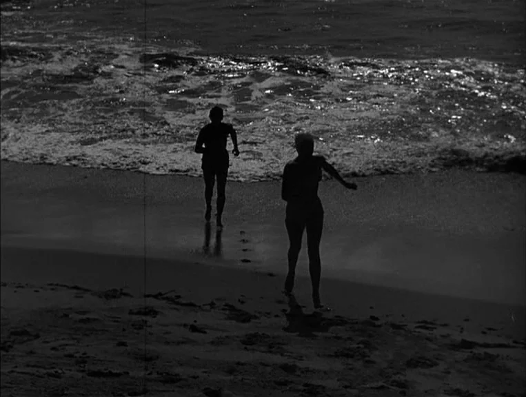 The Postman Always Rings Twice (1946) movie still: fullbody — A dark sand beach with white foam waves crashing against the shoreline. Two people run…