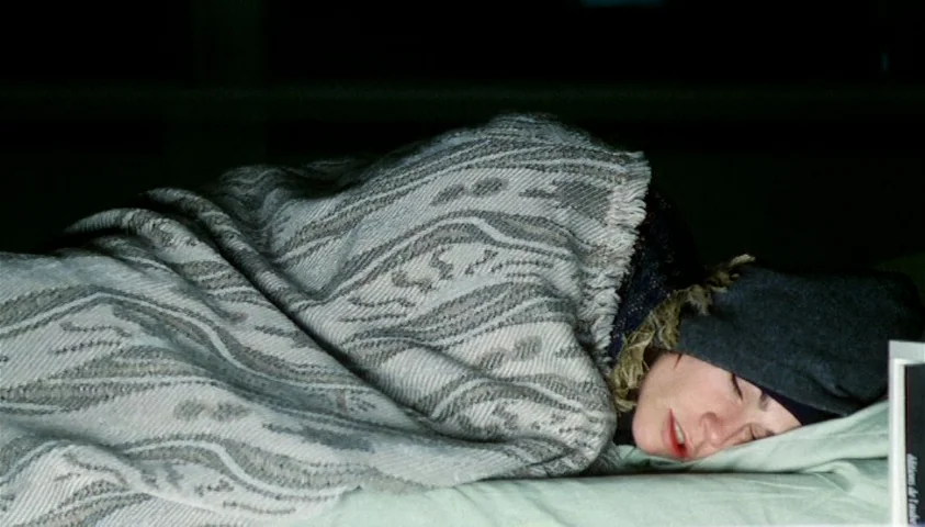 Maelström (2000) movie still: closeup — A dimly lit indoor space with a person lying on a flat surface. The person is wrapped in a textured woven…