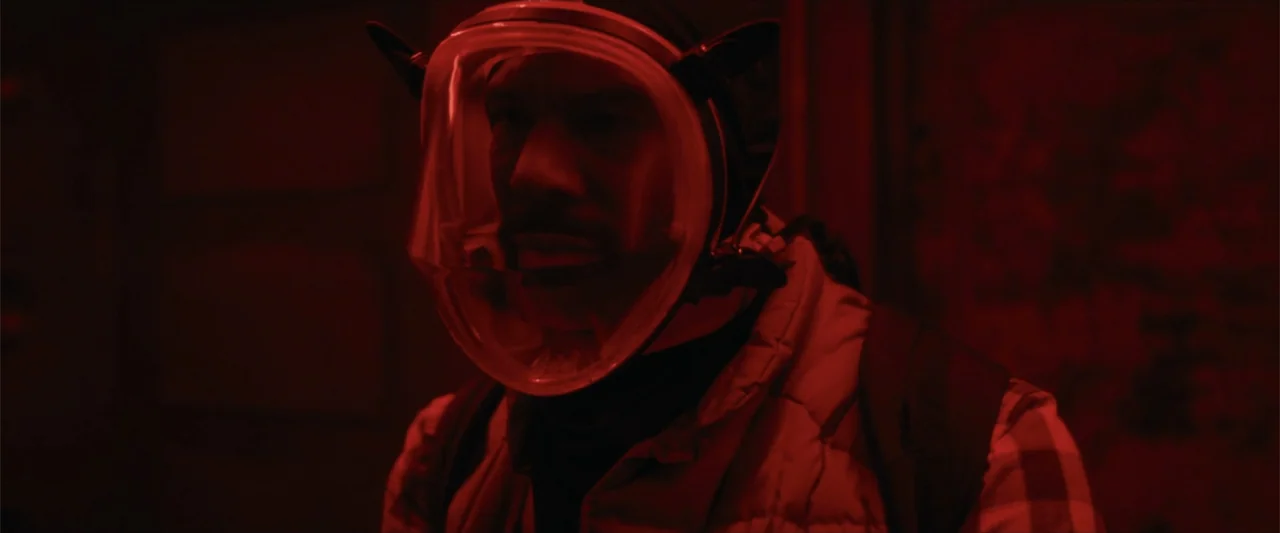 Breathe (2011) movie still: closeup — An interior corridor is dimly lit with deep red light. A man wearing a full-face snorkel-style mask gazes into…