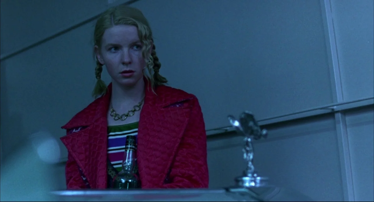 Romper Stomper (1992) movie still: medium — A woman stands in a dimly lit garage featuring a metallic structural wall. She looks toward the right…