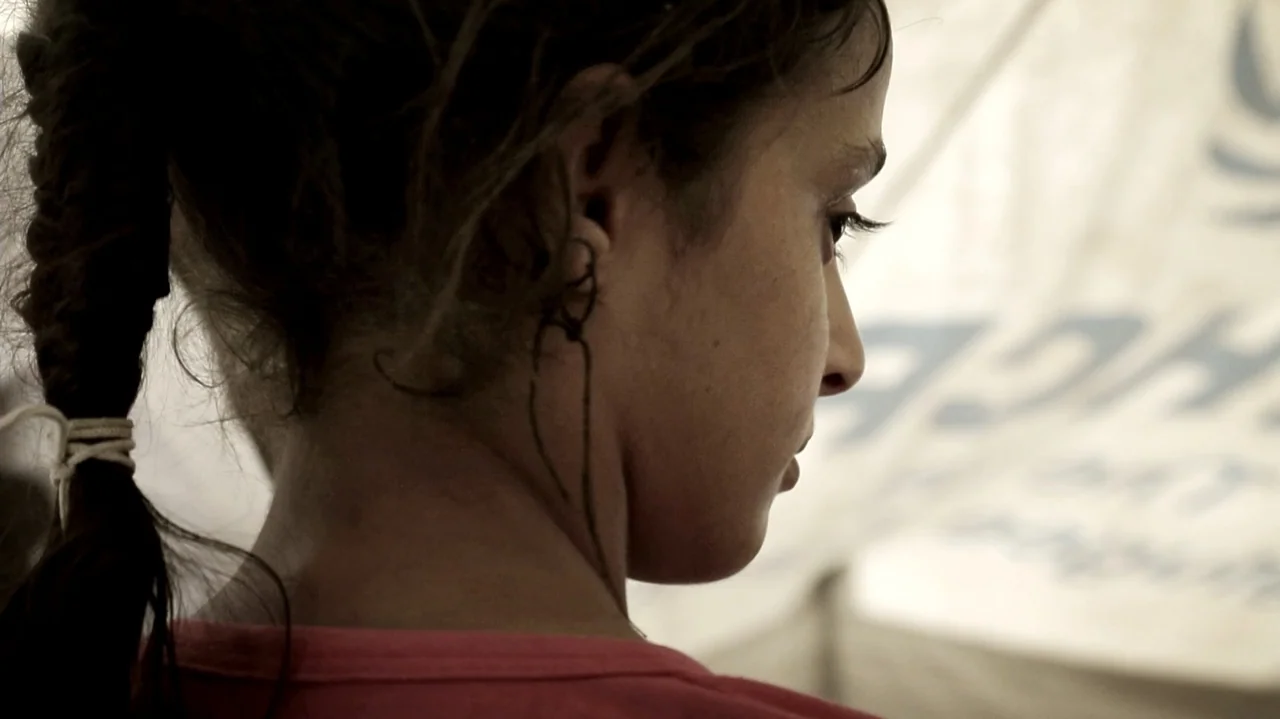City of Two Springs (2019) movie still: closeup — An outdoor area with a white canvas tent wall visible in the blurry background. A young woman…