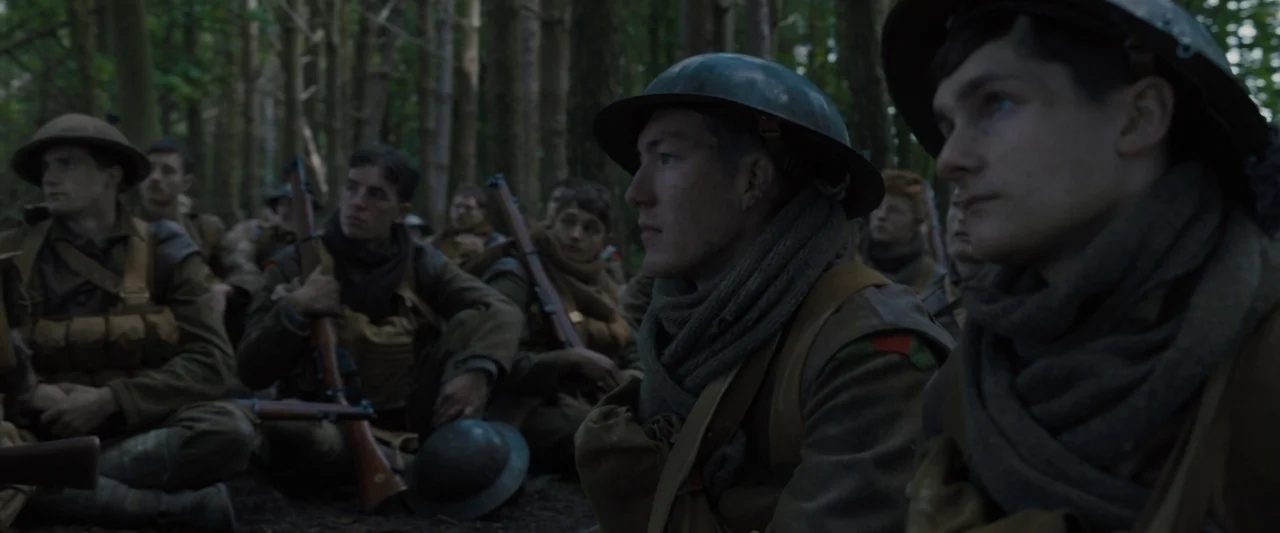 1917 movie still: medium — A group of soldiers in historical uniforms sits amongst dense trees in a forest. Several men wait with their rifles while…