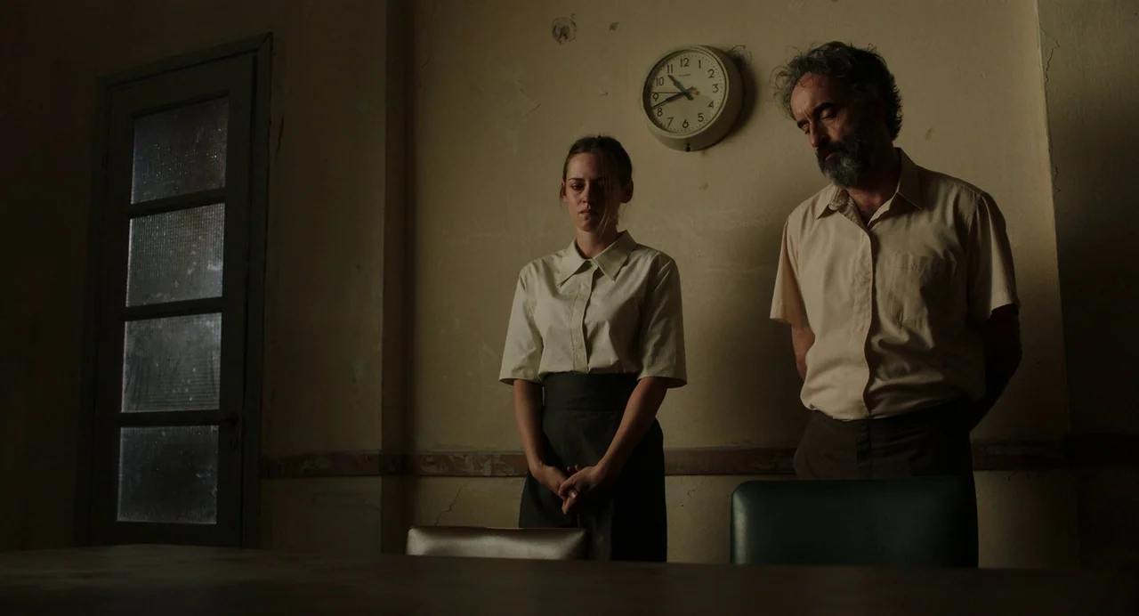 Crimes of the Future (2022) movie still: medium — An interior space with peeling plaster walls features an analog wall clock. Two people stand…