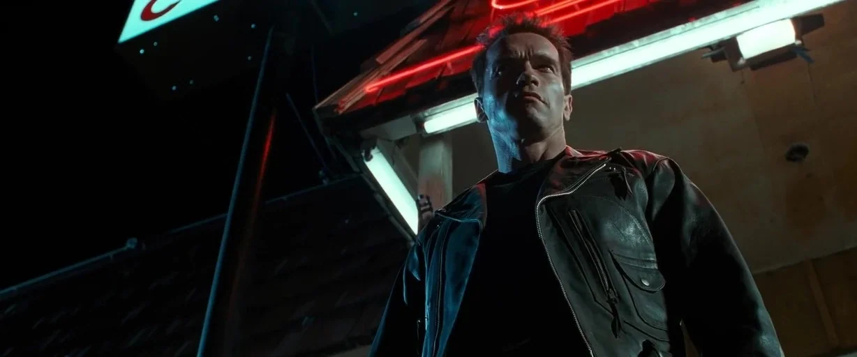 Terminator 2: Judgement Day (1991) movie still: medium — A man stands beneath the metal canopy of a night-time service station. The scene is lit by…
