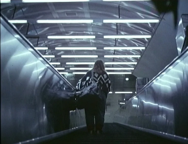 Ghosts… Of The Civil Dead (1988) movie still: A striking shot captures a lone figure ascending a long, brightly lit escalator in an underground…