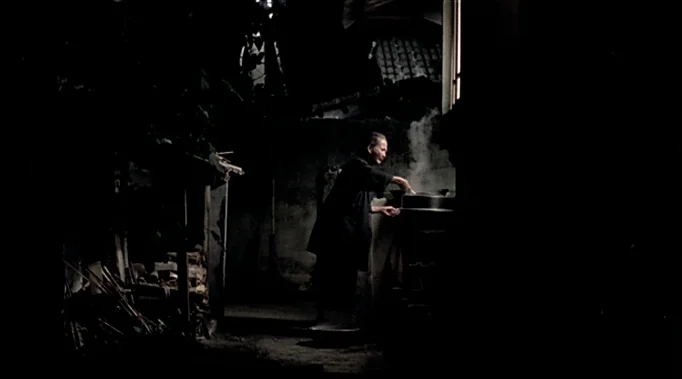 A Time To Love and A Time To Die (1985) movie still: wide — A dark night courtyard features an elderly man preparing food over an outdoor fire.…