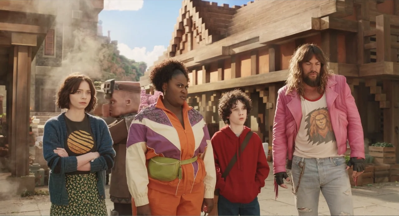 A Minecraft Movie (2025) movie still: fullbody — A blocky stylized village made of square wooden beams and pixelated architecture. Four distinct…