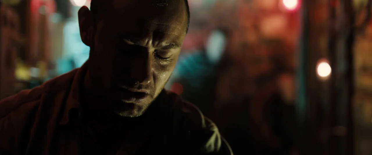 Black Sea (2014) movie still: closeup — A dimly lit interior space features blurred neon lights and soft out-of-focus background textures. A man in…