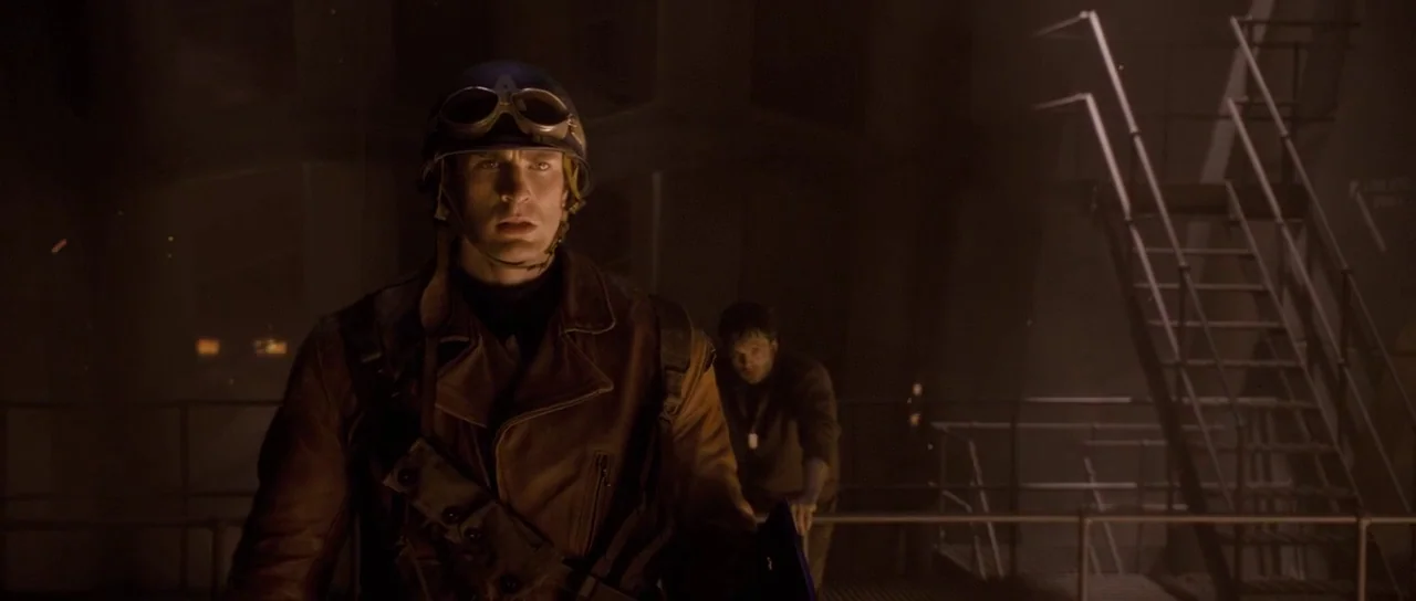 Captain America: The First Avenger (2011) movie still: medium — A dimly lit industrial environment features metal railings and a staircase in the…
