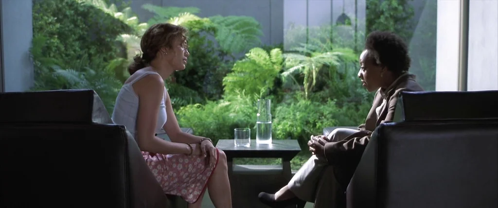 The Cell (2000) movie still: medium — A modern interior space features two black leather chairs facing a windowed atrium. Two women sit across from…