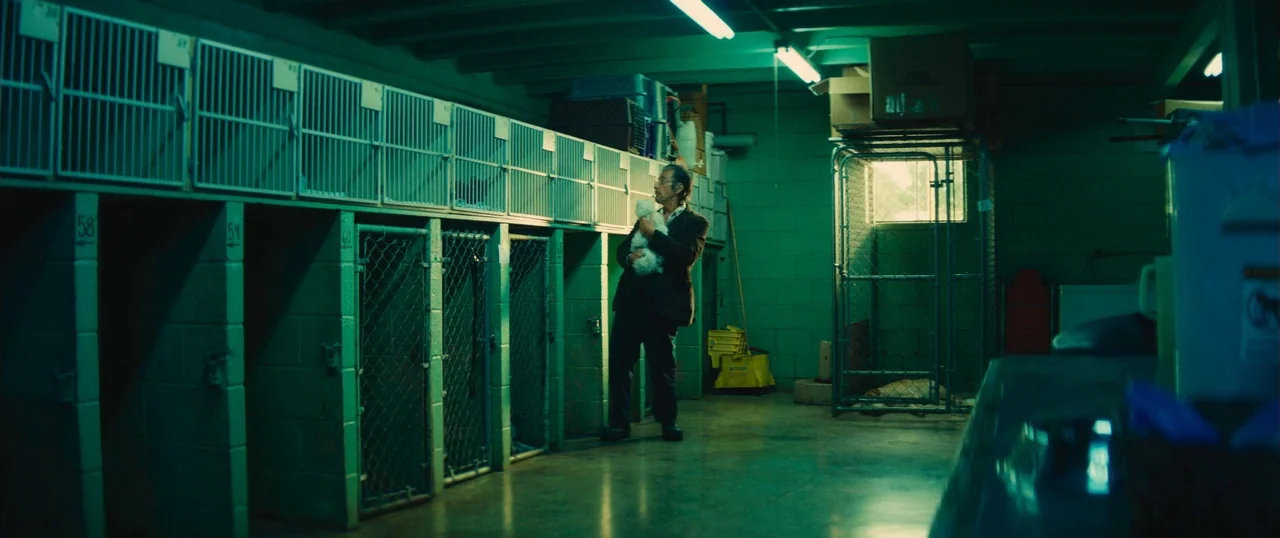 Manglehorn (2014) movie still: wide — A rows of wire cages line a windowless concrete room illuminated by fluorescent lights. An older man stands in…