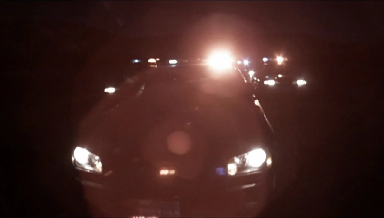 Dark Country (2009) movie still: medium — A vehicle sits on a dark road at night with its bright headlights activated. The front of the car is…