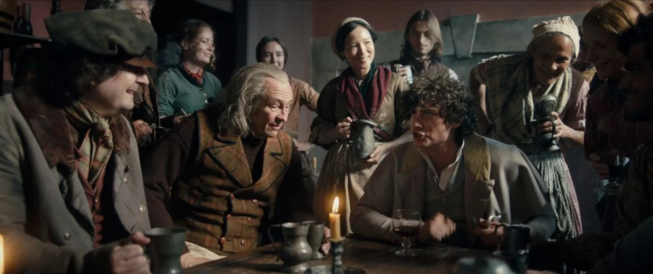 The Personal History of David Copperfield (2019) movie still: medium — A dimly lit room with stone walls occupied by people around a wooden table.…