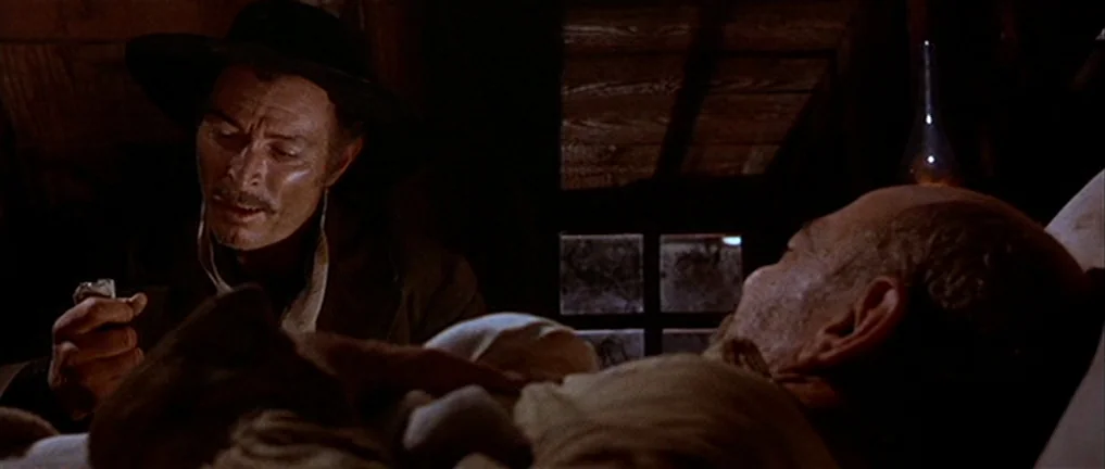 The Good, The Bad And The Ugly (1966) movie still: medium — A dimly lit attic with wooden sloped rafters serves as a quiet space. A man in a hat…