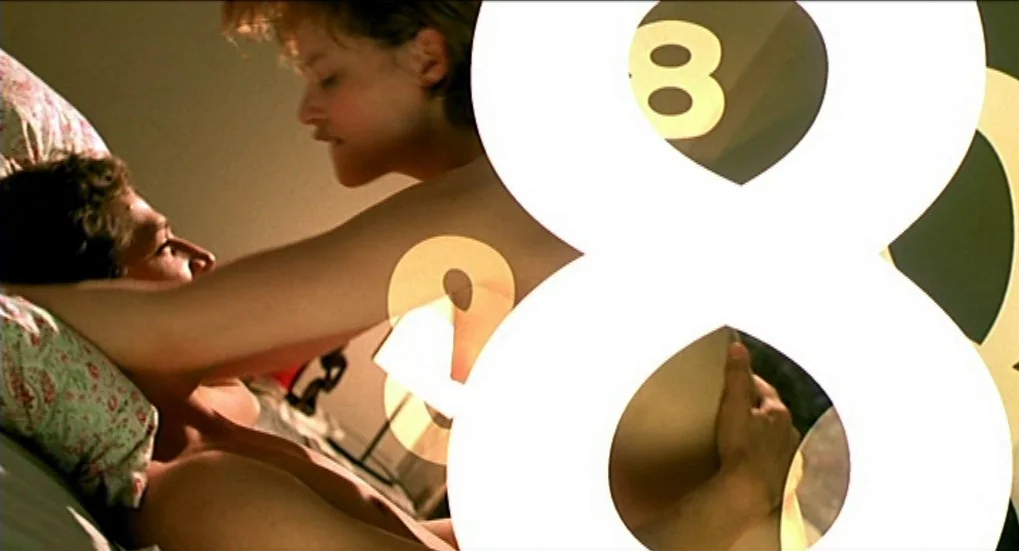 Jeux d’Enfants (2003) movie still: medium — A dark bedroom interior shows two individuals lying close together on a bed. The foreground is partially…